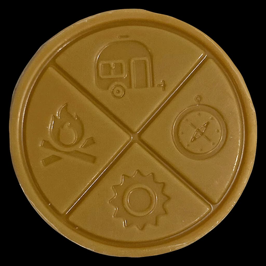 Laughing Ass Caramel Gold Full Spectrum THC chocolate with embossed icons representing adventure, navigation, camping, and fire on tan-colored round disk